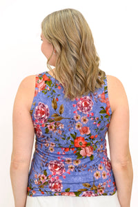 Back view of woman wearing blue sleeveless top with pink flowers and white pants against a white background