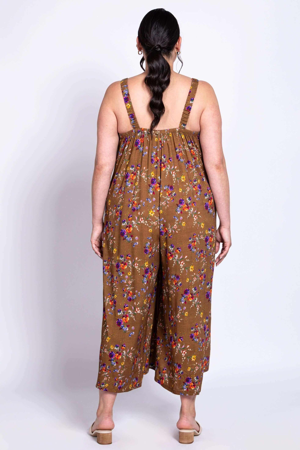 Person showing the back of a brown floral jumpsuit with wide legs and elastic straps