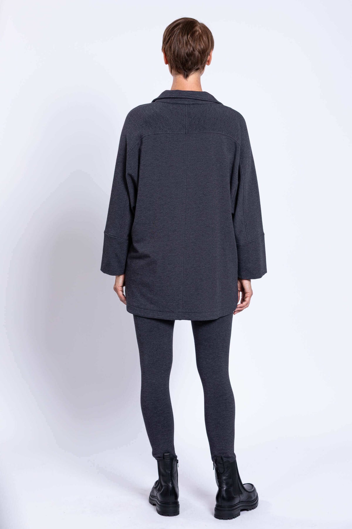 Rear view of a woman wearing a dark grey dolman sleeve jacket and leggings