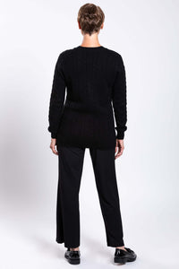 Rear view of a woman in a black cable knit cardigan and black pants