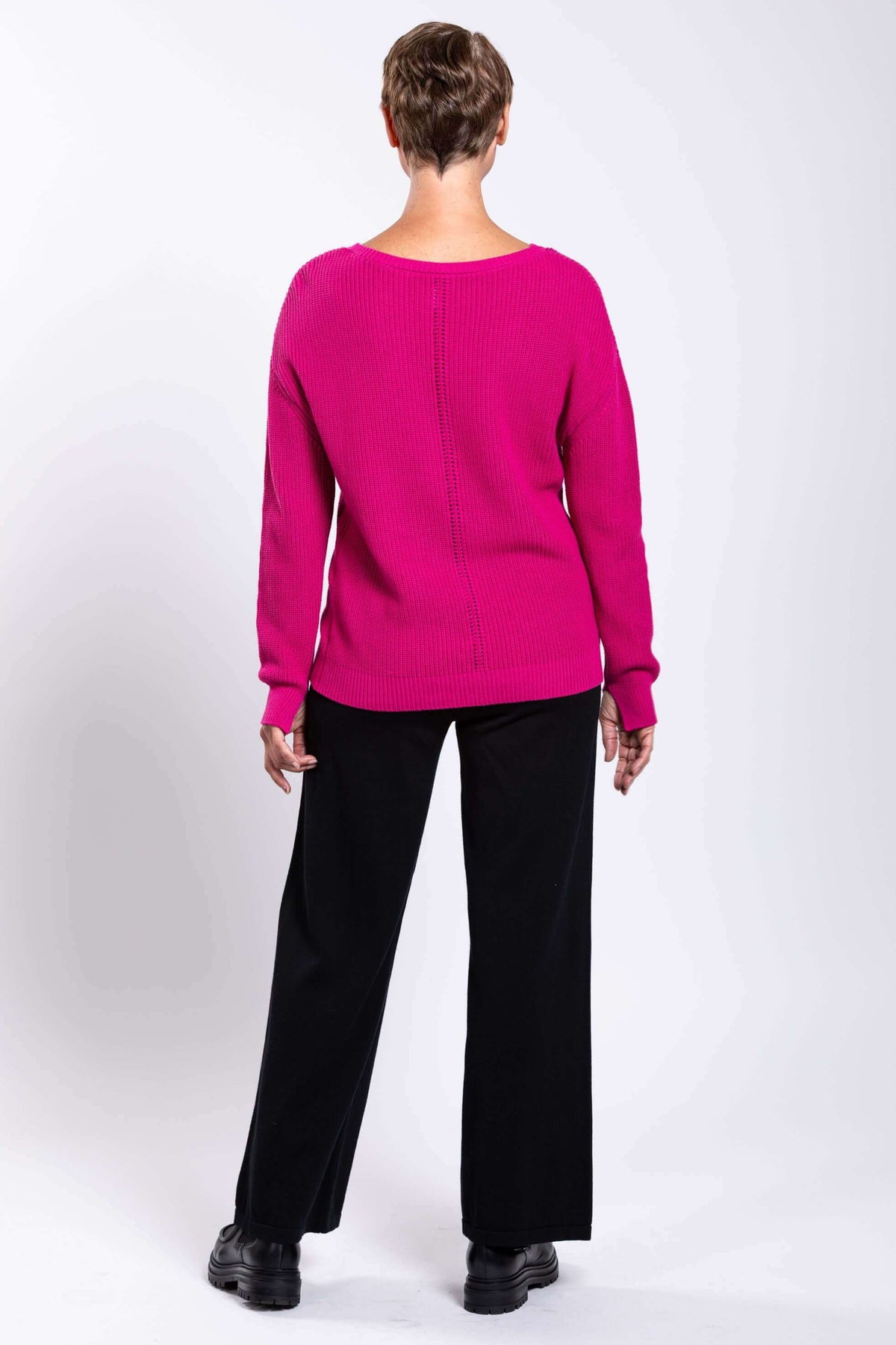 Rear view of a woman wearing a fuchsia pink shaker stitch sweater and black pants