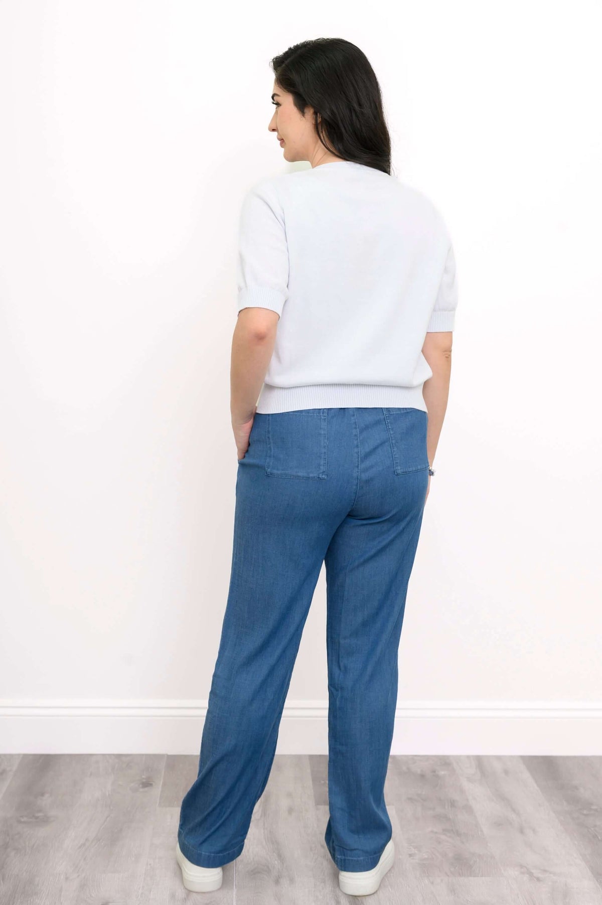 Back view of woman wearing light short-sleeve cardigan and blue pants