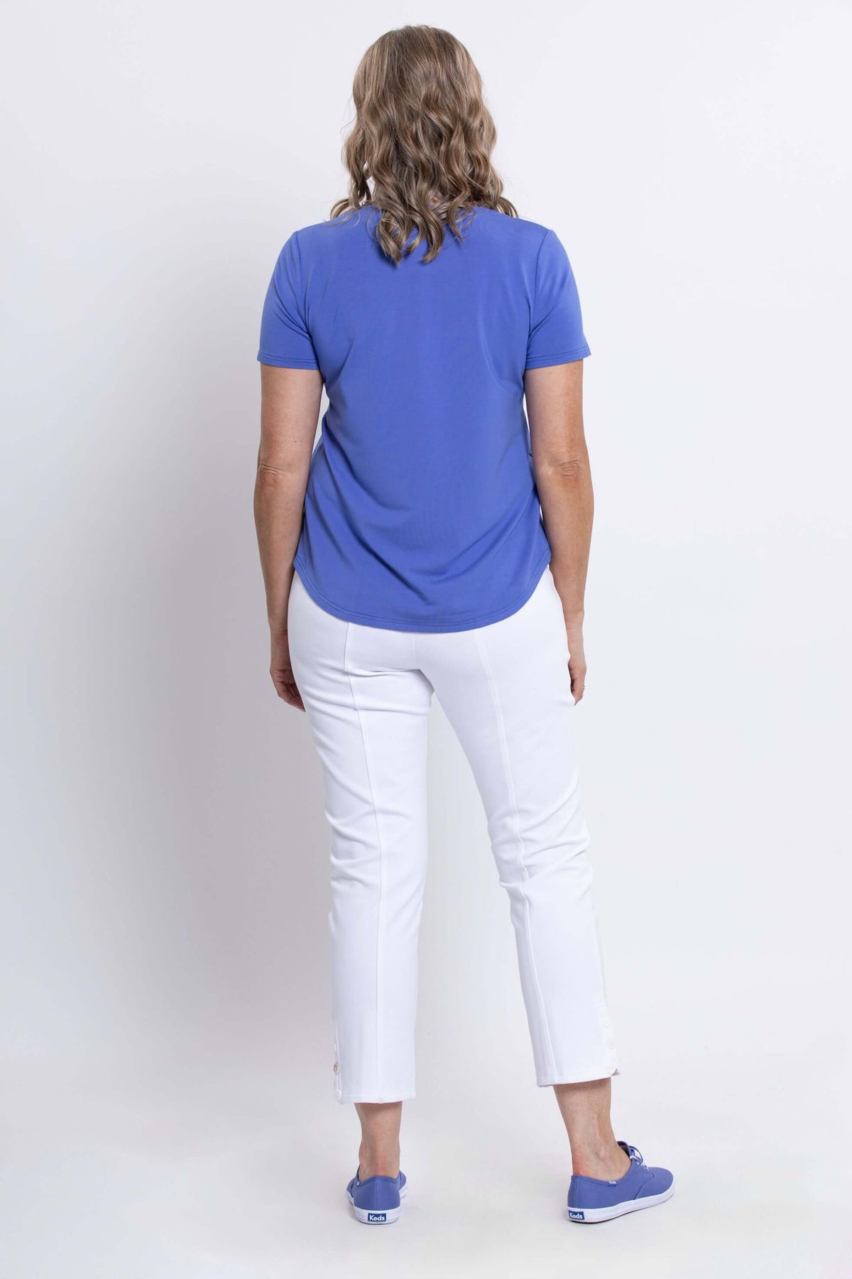 Rear view of woman wearing blue Tessa Tee with white pants and blue sneakers