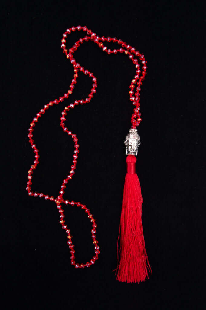Red crystal mala necklace with Buddha head pendant and red tassel displayed on a black background