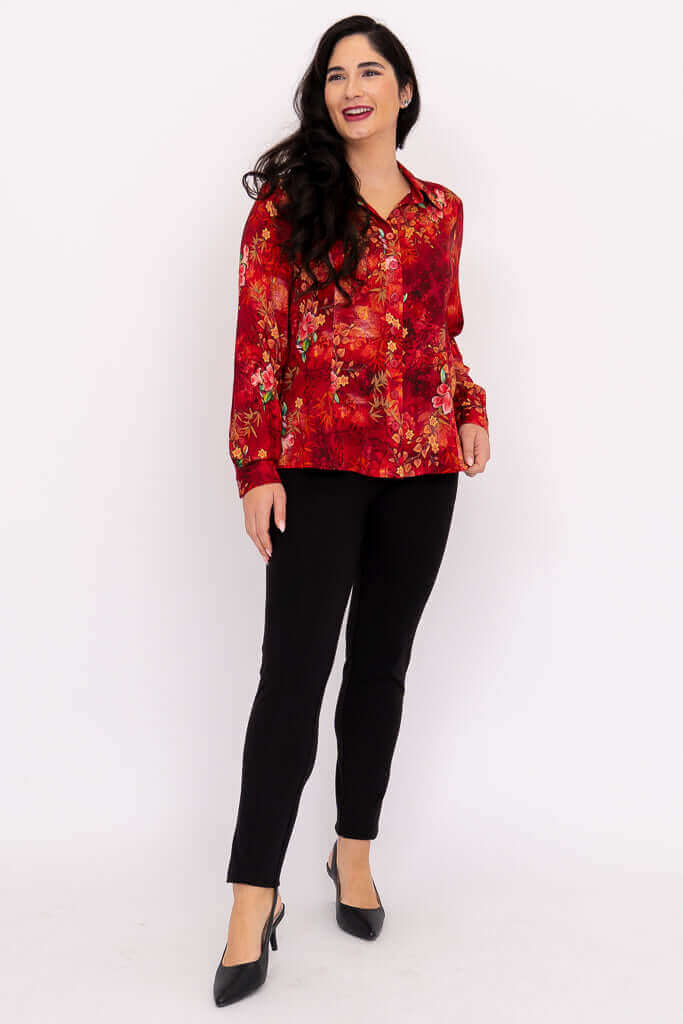 Woman standing and smiling in a red floral long-sleeve blouse paired with black pants