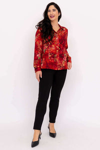 Woman standing and smiling in a red floral long-sleeve blouse paired with black pants