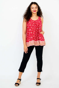 Woman in a red floral pleated tank top and black pants, standing front view