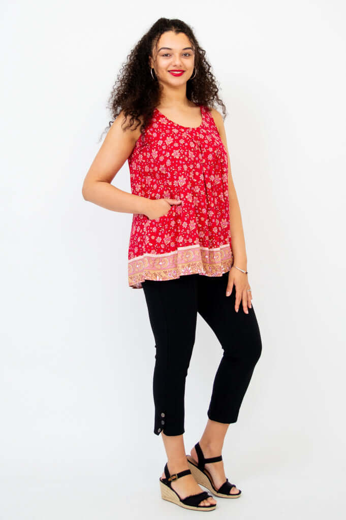 Smiling woman in a red floral tank top with her hand in the pocket, angled view