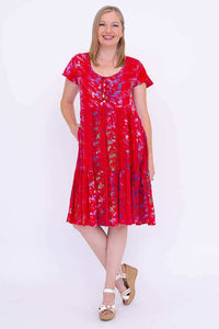 Woman standing with legs crossed, wearing a red floral tiered dress and white wedges