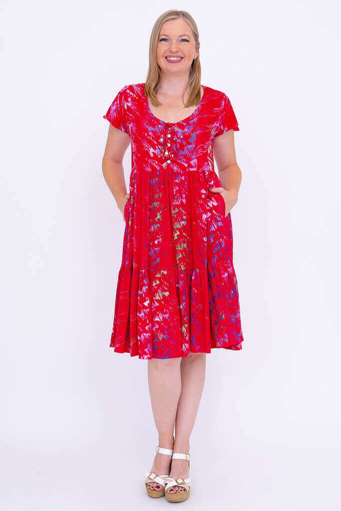 Woman wearing a red flutter sleeve tiered dress with a floral print, standing and smiling