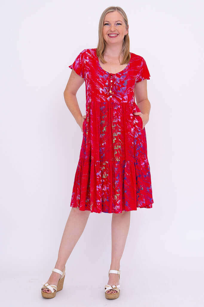 Woman posing with hands in pockets, wearing a bright red tiered dress with flutter sleeves