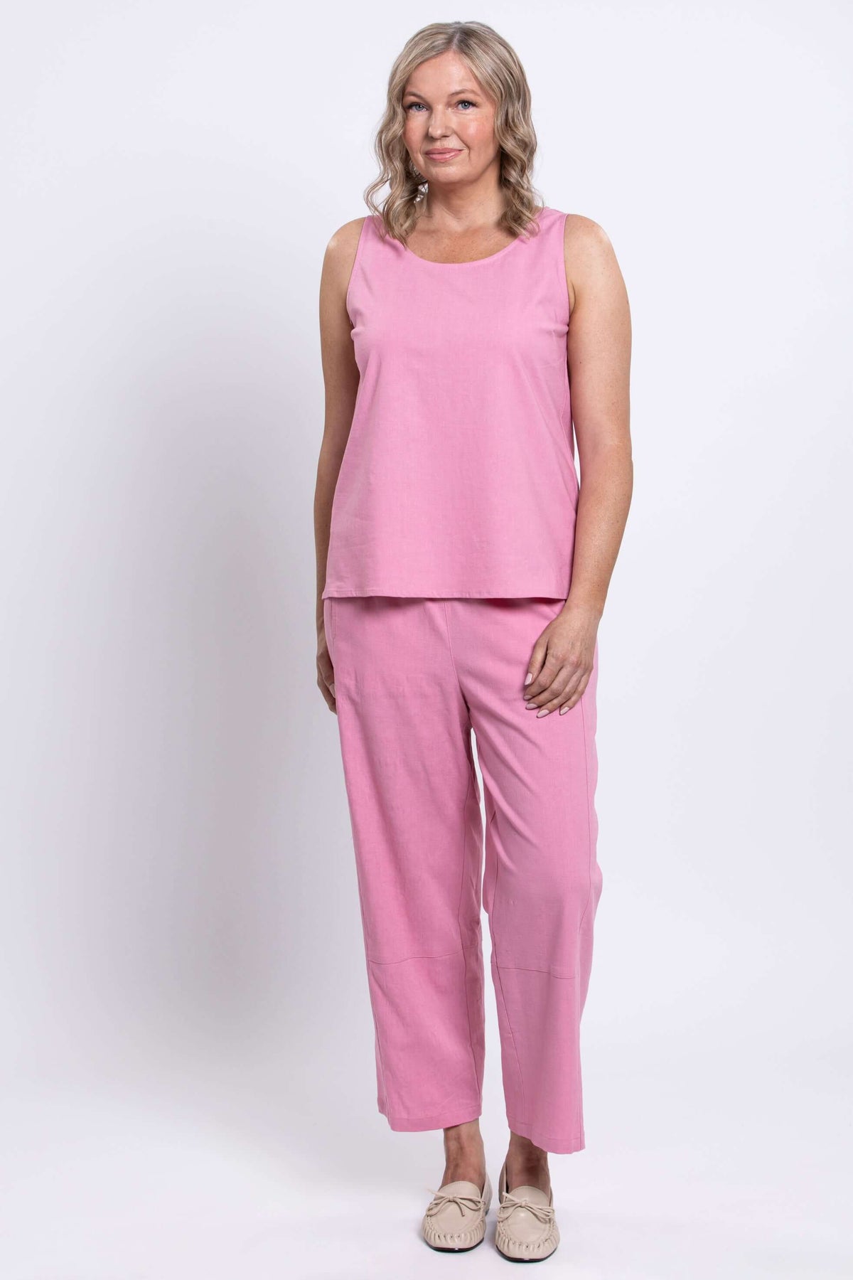 Woman in pink sleeveless top and cropped pants, standing with a relaxed pose, front view