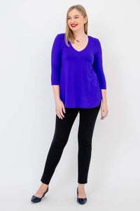 Woman standing with one leg crossed in purple V-neck bamboo top, looking to the side