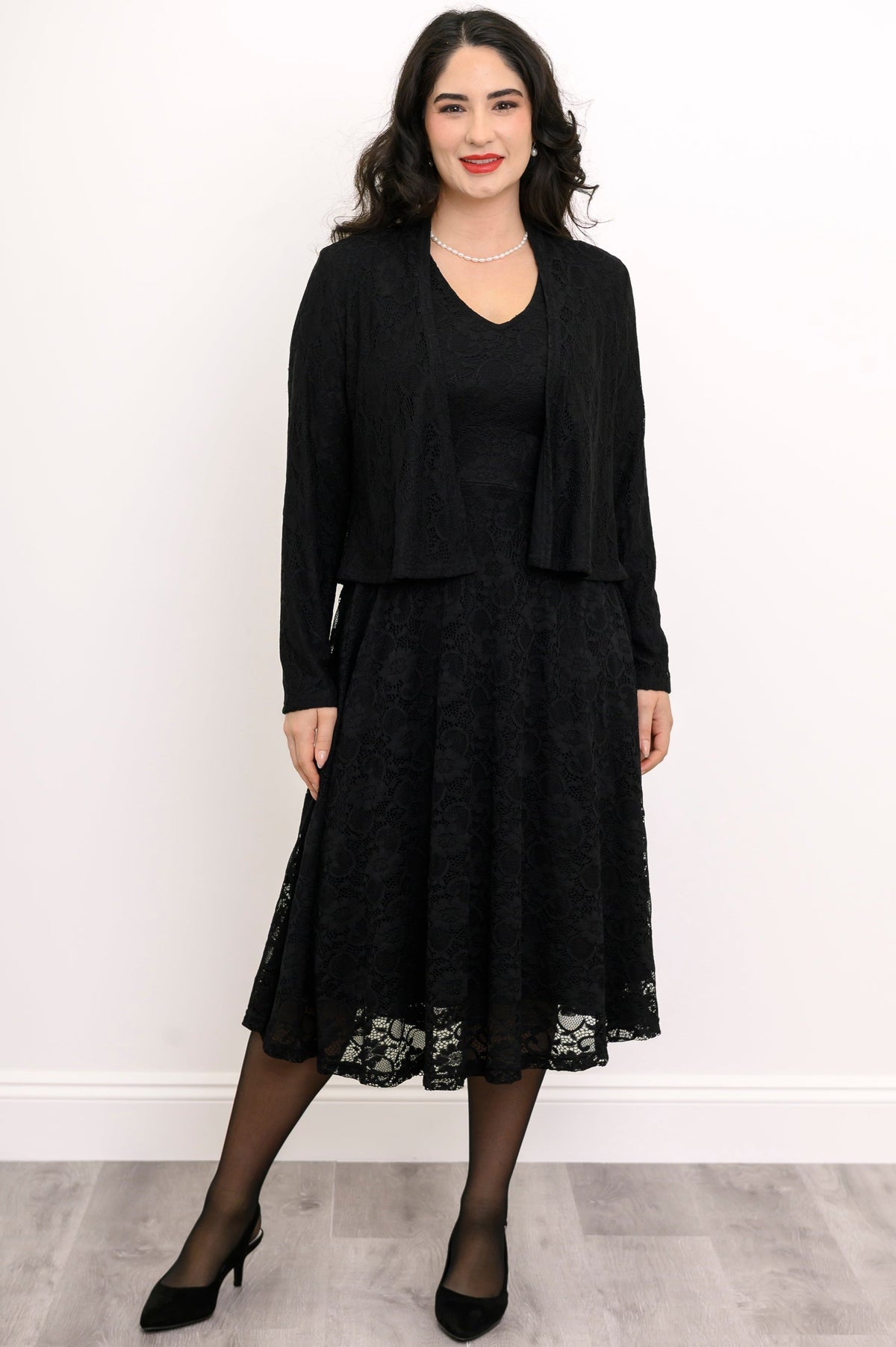 Woman wearing a black lace dress with a matching jacket against a white background, front view