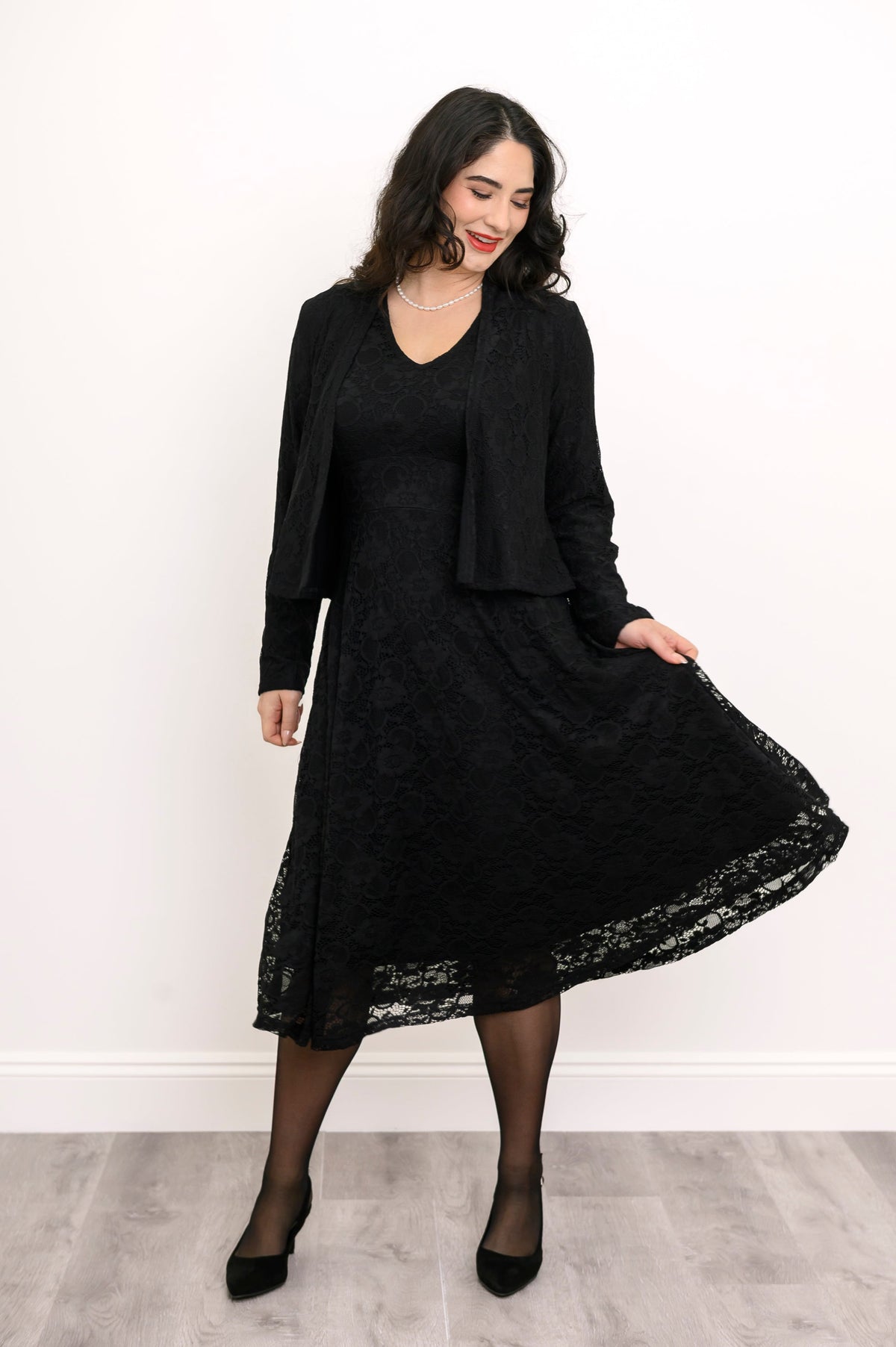 Woman playing with the hem of her black lace flared dress, smiling