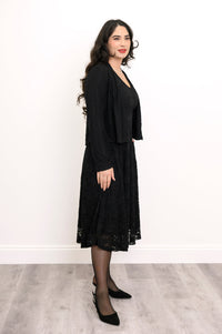 Side view of woman wearing loose-fit black dress with lace overlay and matching cardigan
