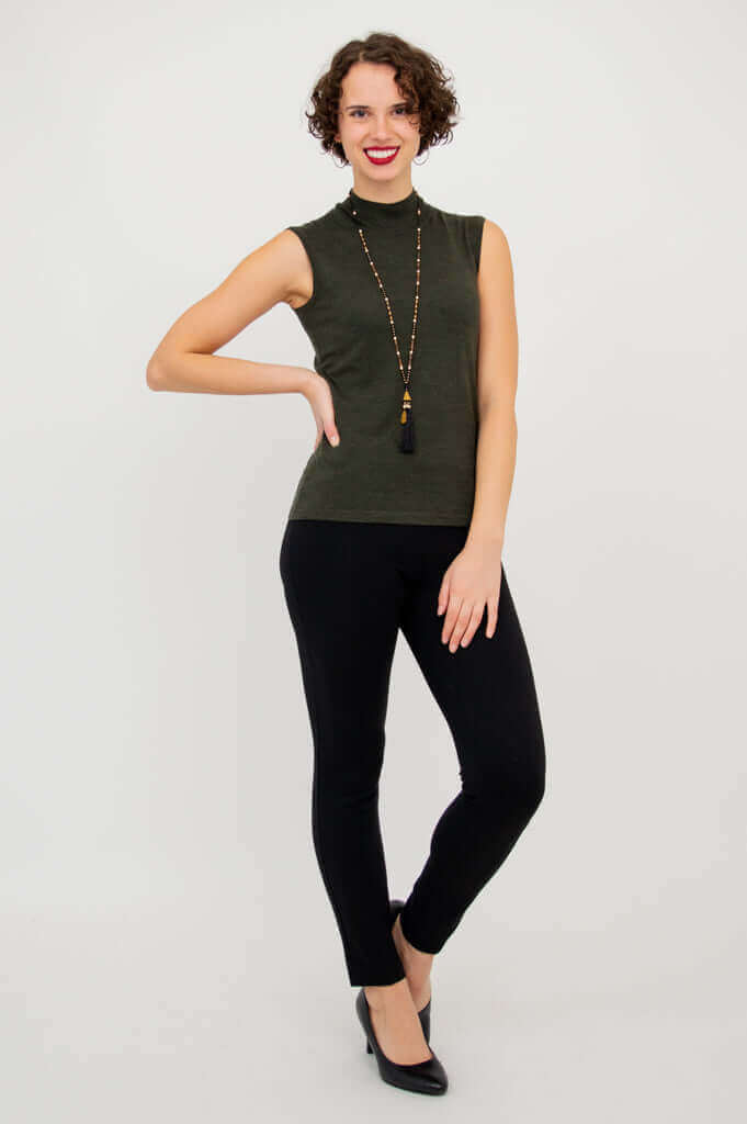 Woman in olive-green sleeveless mock neck sweater and black pants, hand on hip, full body