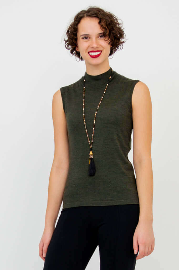 Woman smiling in sleeveless olive-green mock neck sweater and long beaded necklace