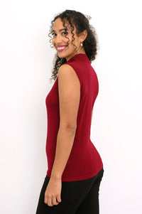 Side profile view of a woman wearing a sleeveless burgundy merino wool top styled with black pants.