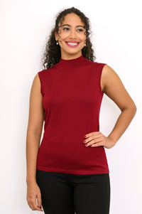 Full length view of a woman wearing a slim fit burgundy sleeveless merino wool knit top with black pants.