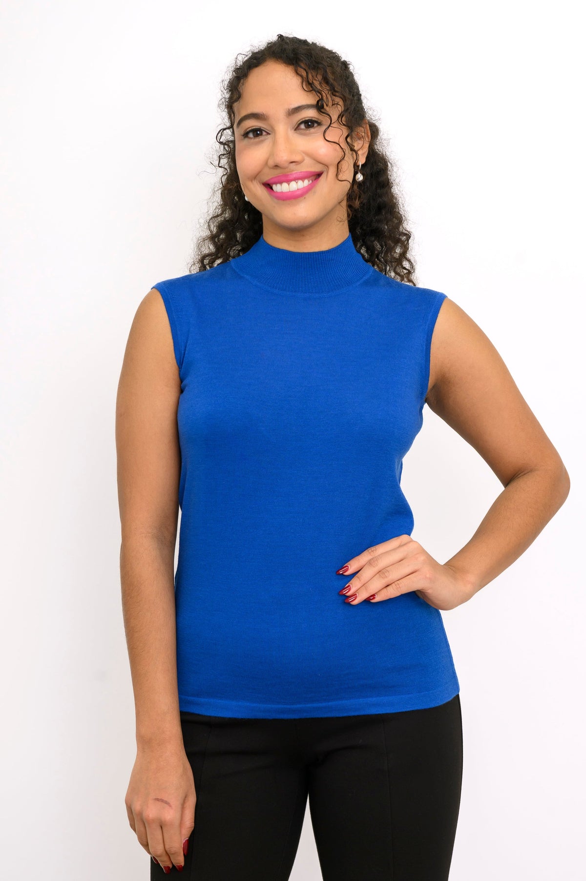 Woman modeling a hip length cobalt blue sleeveless mock neck knit top with black trousers.
