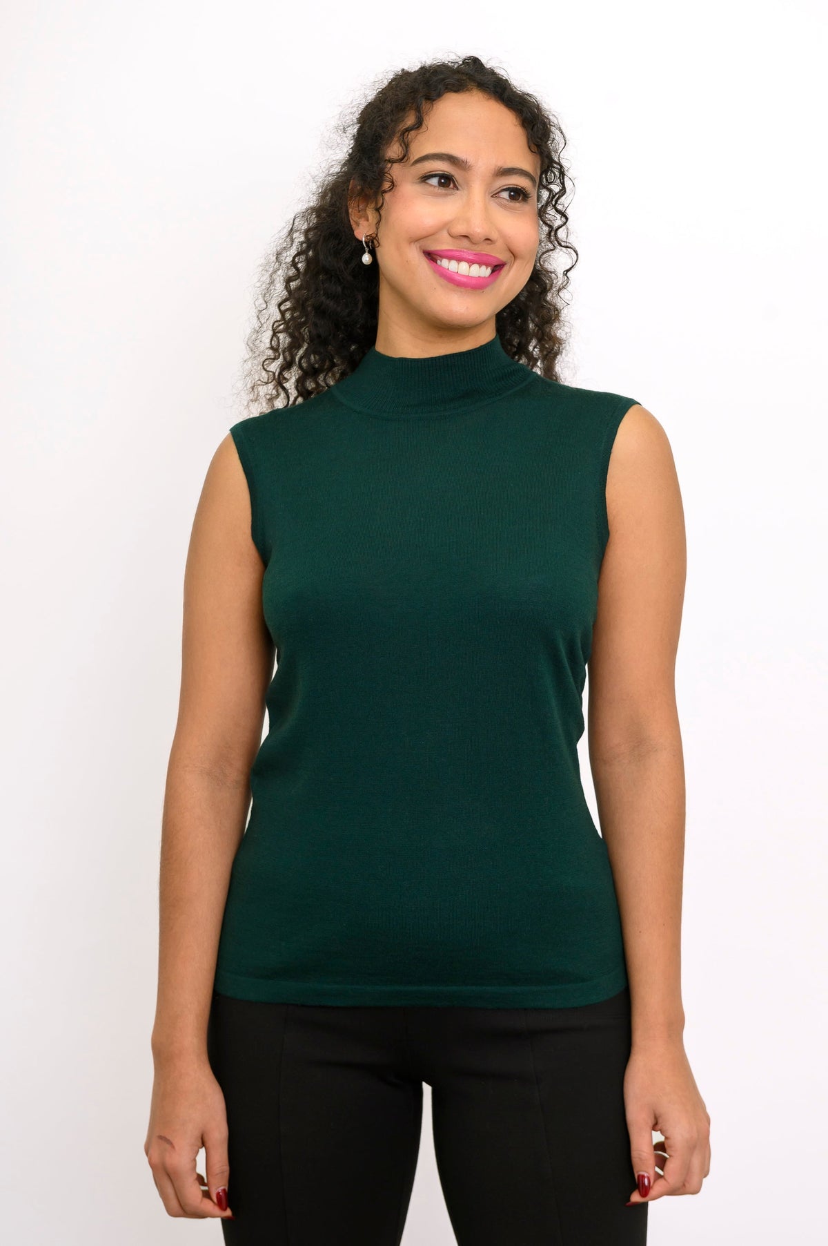 Front view of a woman wearing a comfortable dark forest green sleeveless knit top on a white backdrop.