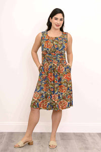 Woman modeling floral dress with ruched bodice and hands in pockets, three-quarter view