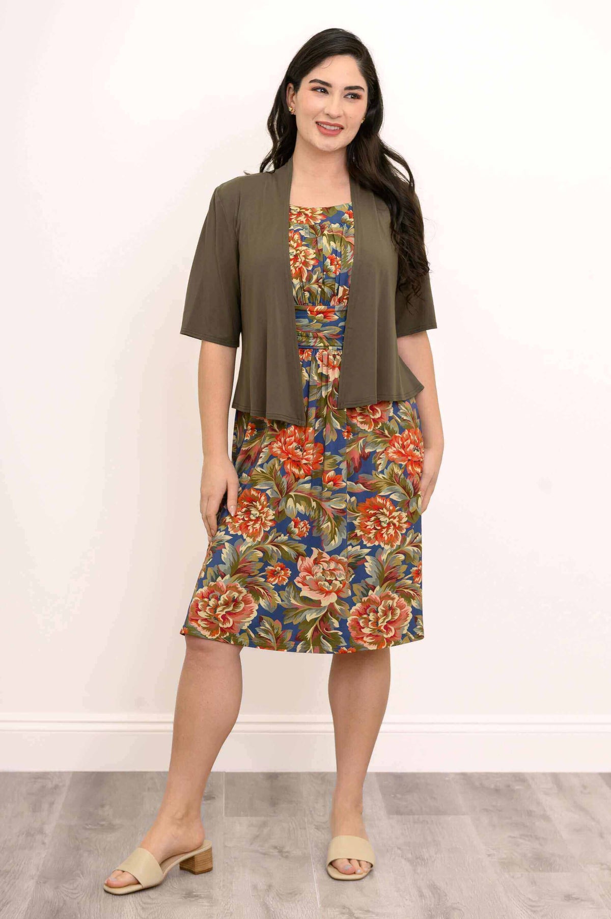 Woman wearing floral dress with ruched bodice and olive green jacket, front view