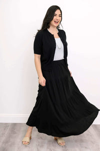 Woman twirling in black tiered maxi skirt, styled with short-sleeve cardigan