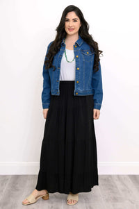 Woman in black tiered maxi skirt with white top, denim jacket, and green necklace
