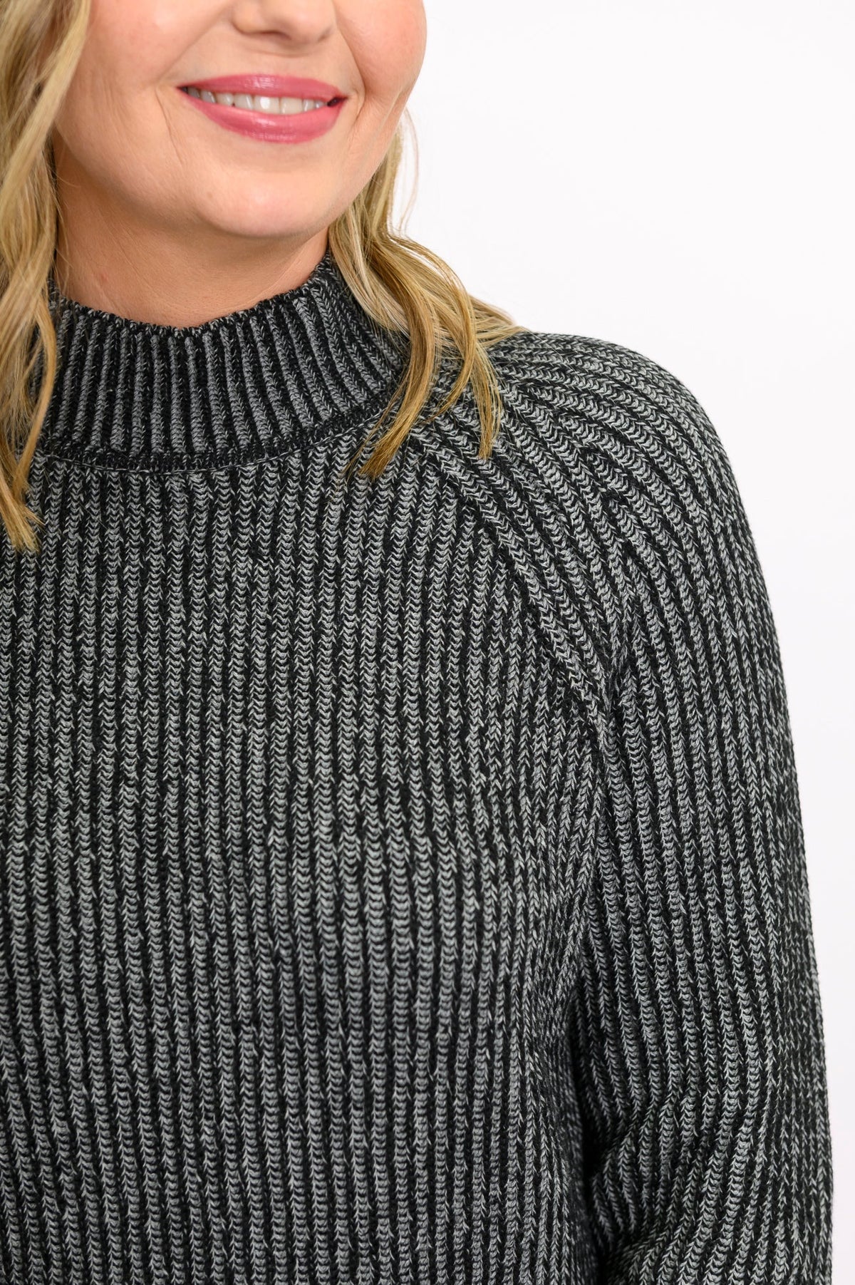 Close-up of a charcoal gray cotton sweater, highlighting the textured two-tone stitch and low mock neck collar.