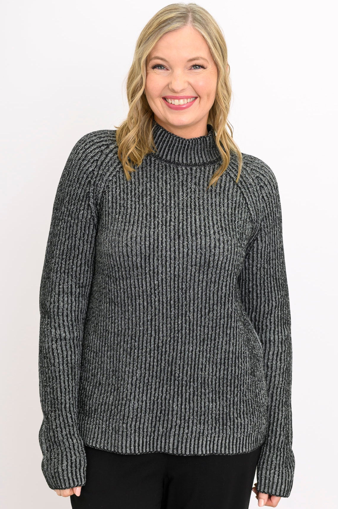 Smiling woman wearing a chunky charcoal gray knit sweater with a low mock neckline and relaxed raglan sleeves.