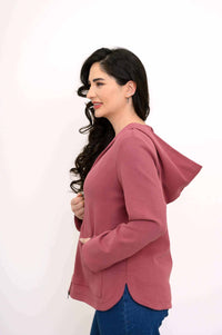Woman shown from the side, displaying the hood and curved hem of a rose zip-up jacket