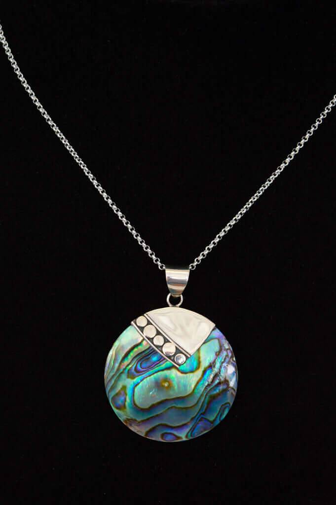 Close-up of round abalone shell pendant necklace with sterling silver chain on black background