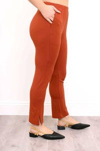 Side view of rust bamboo pants paired with black flats, showing slim fit and slit