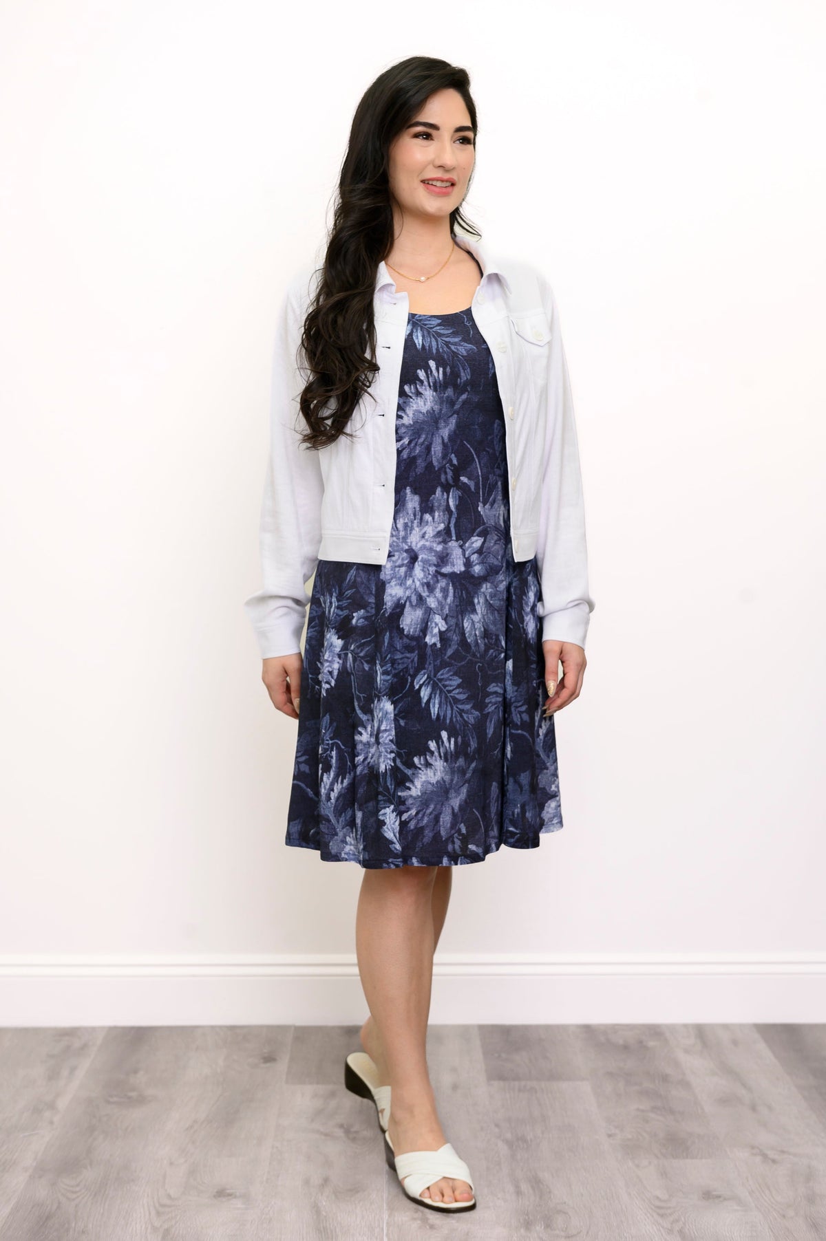 Woman wearing a floral blue dress and white jacket facing slightly away from the camera