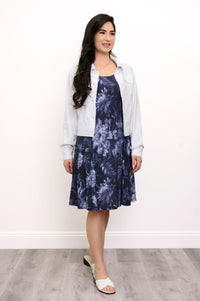 Woman wearing a floral blue dress and white jacket facing slightly away from the camera