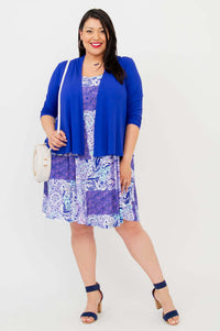 Woman wearing a purple dress with blue cardigan and white shoulder bag, front view