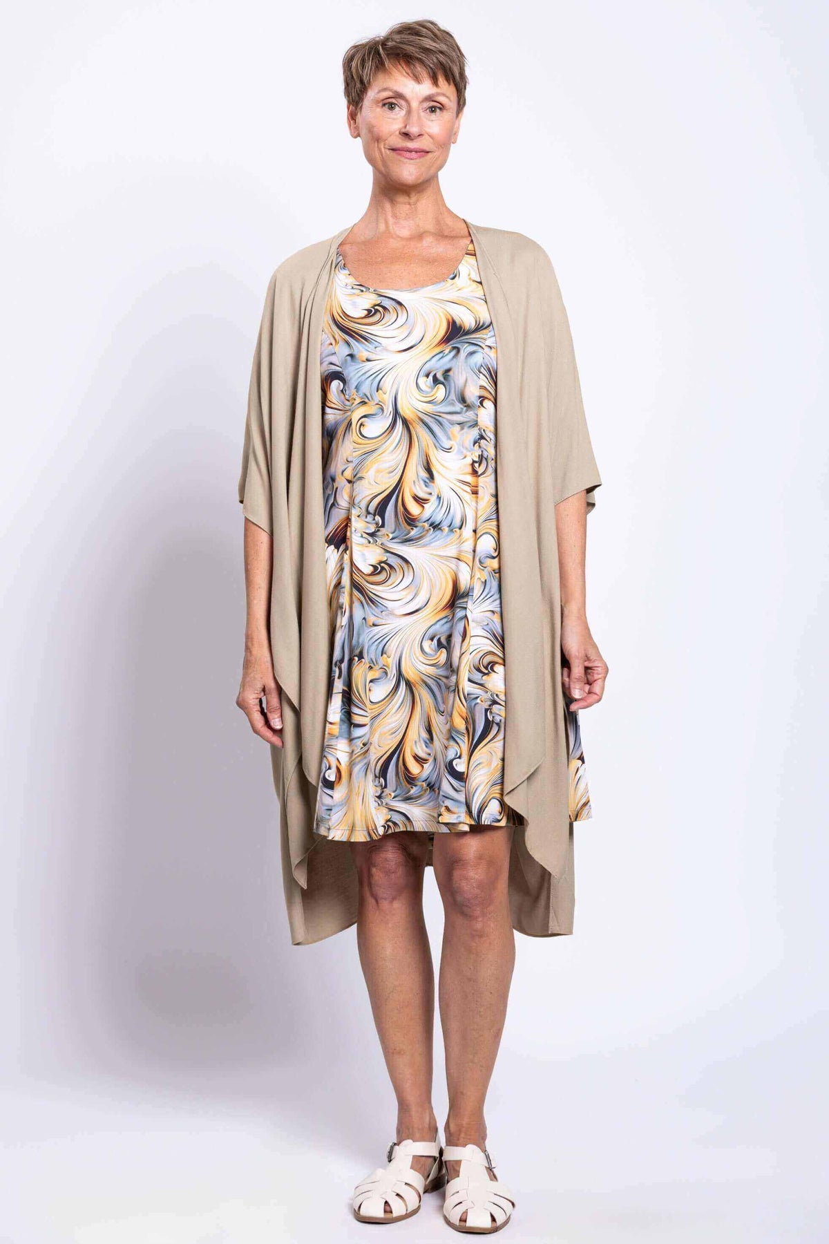 Model in swirl print dress with taupe open-front cardigan and white sandals