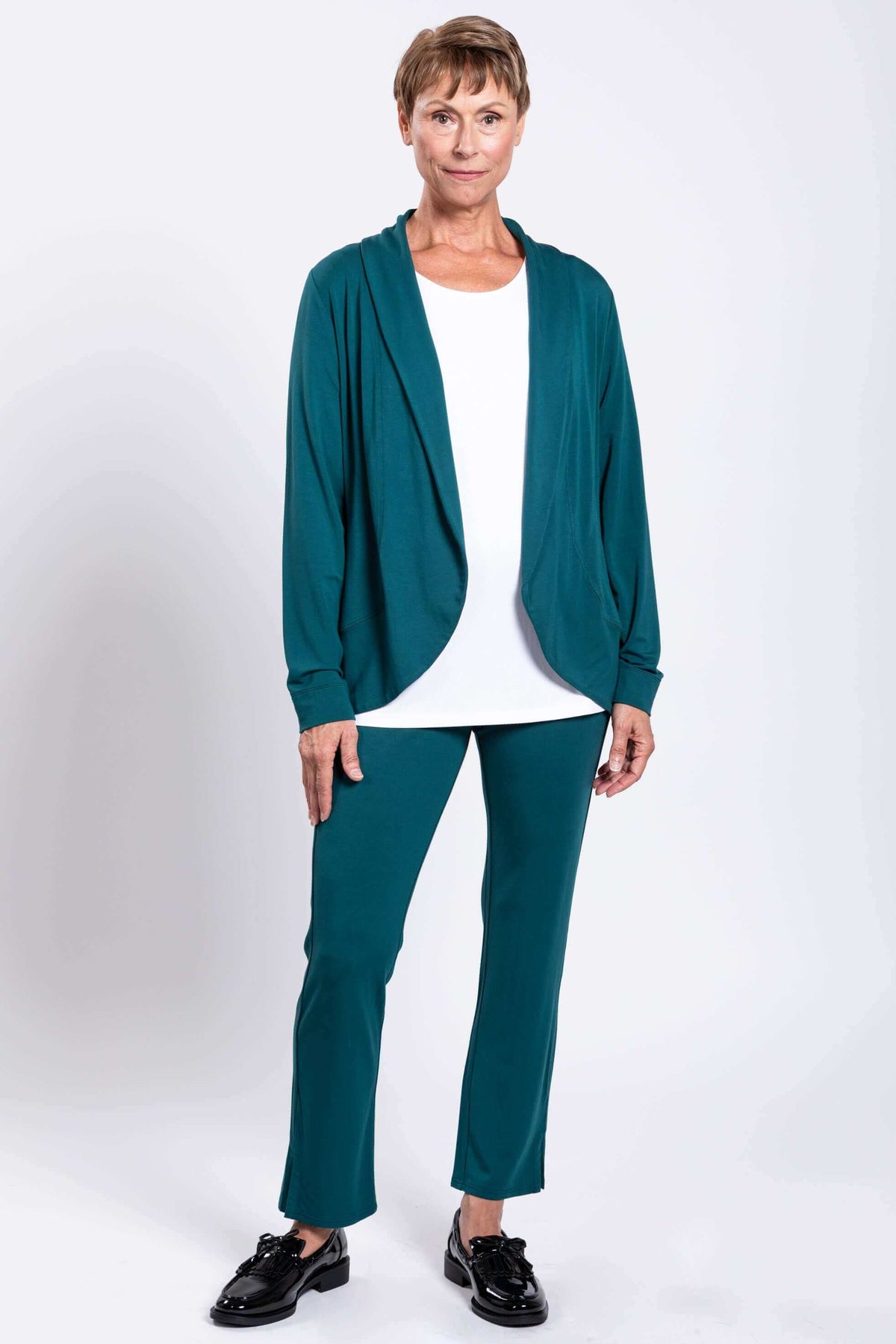 Front view of woman wearing teal jacket on a white top and teal pants with ankle slit and sneakers