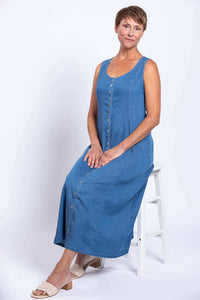 Woman seated, wearing a sleeveless blue Tencel denim maxi dress with button front