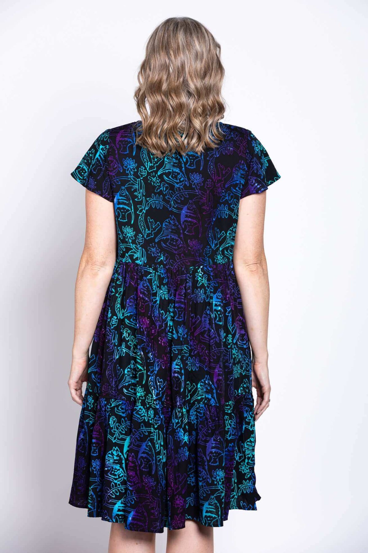 Back view of dress with blue and purple botanical print and flutter sleeves, model's hair curled