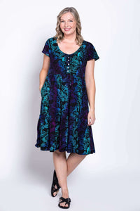 Model smiling in black dress with blue and purple floral print, showing front details and pockets