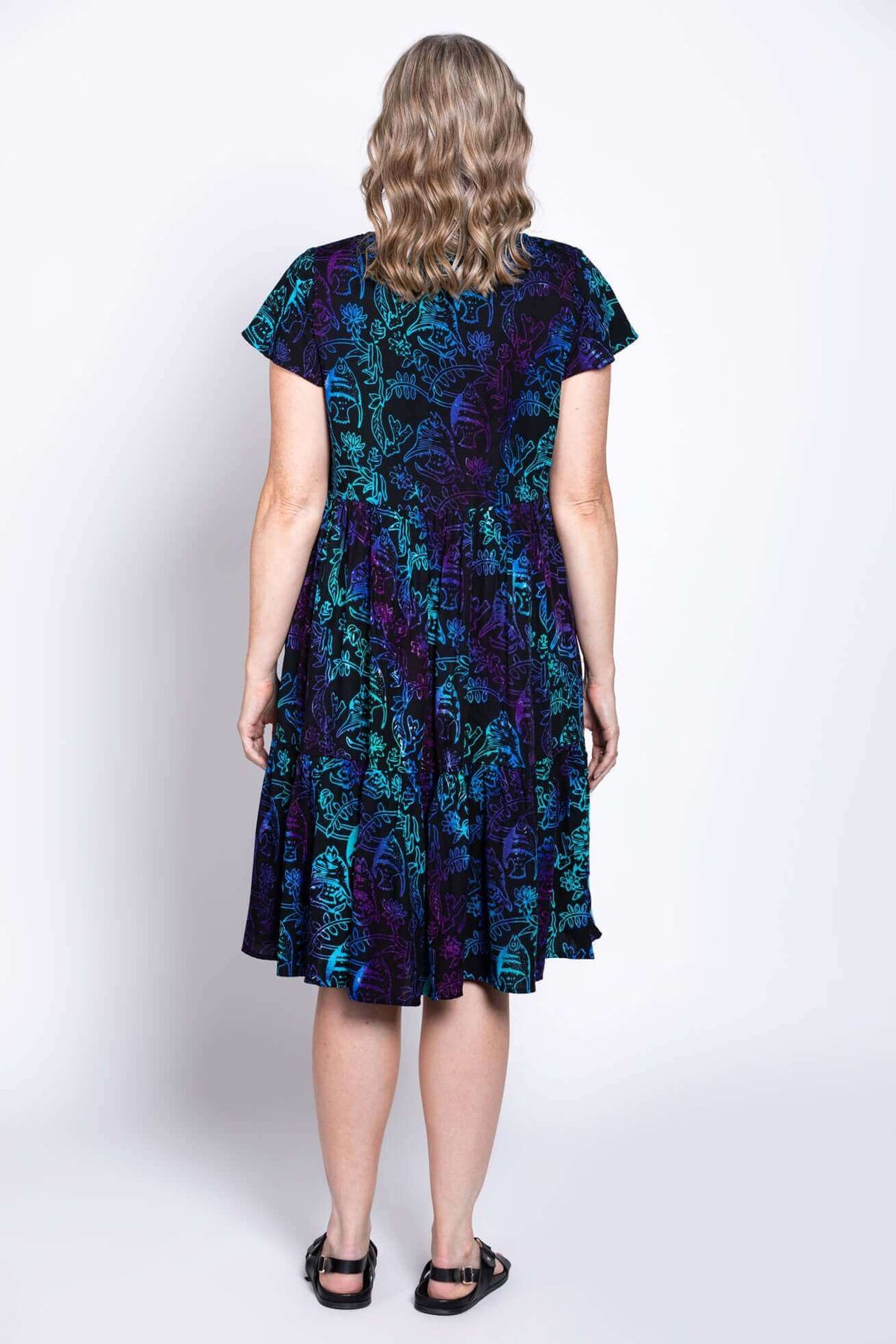 Full back view of model wearing black dress with blue and purple print, flared tiered skirt