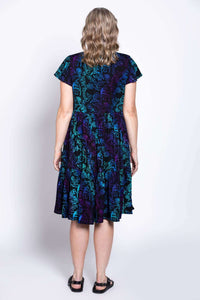 Full back view of model wearing black dress with blue and purple print, flared tiered skirt