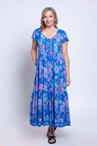 Woman standing with hands in pockets, showcasing the blue floral Sharpie maxi dress