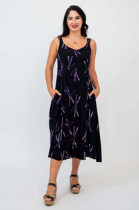 Woman wearing sleeveless black midi dress with purple dragonfly print, hands in pockets