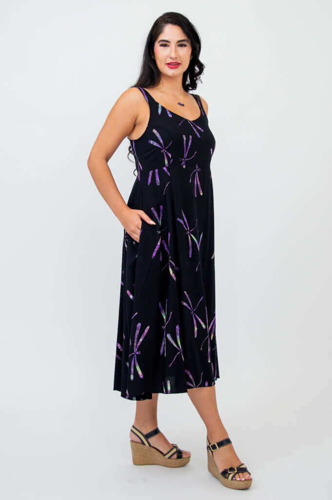 Side view of woman in sleeveless black dress with purple dragonfly print and pockets