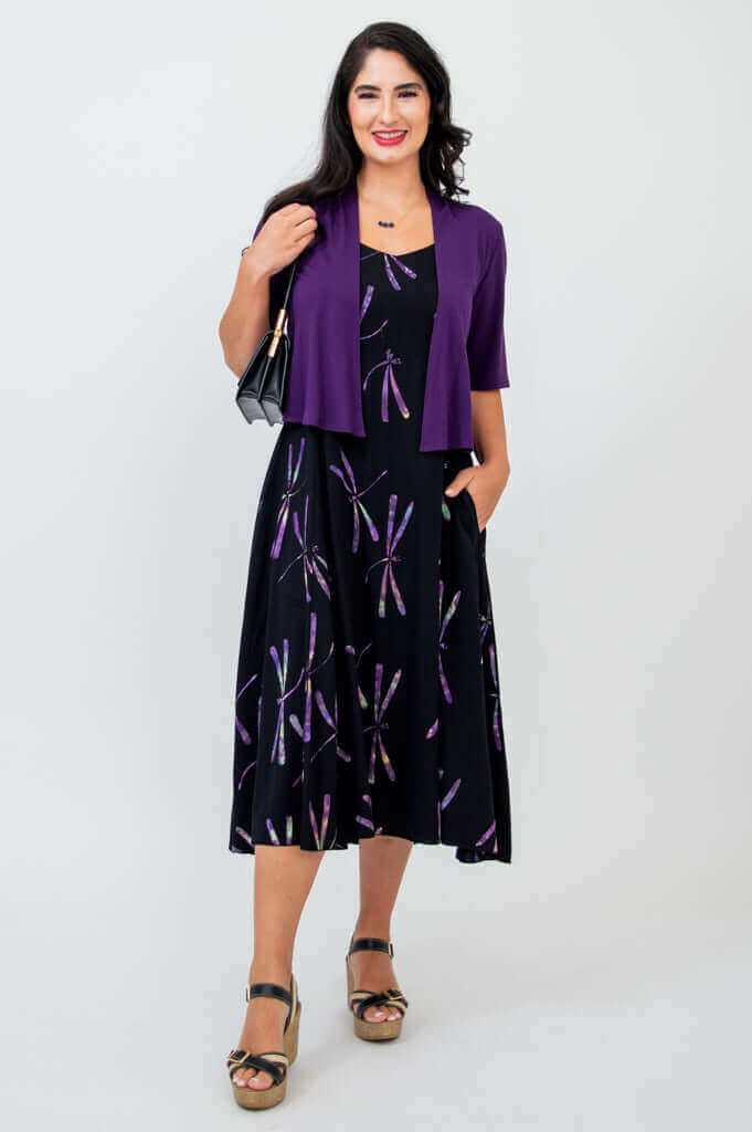 Woman wearing black dragonfly print dress paired with purple shrug and handbag