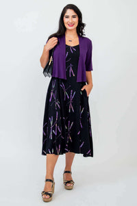 Woman wearing black dragonfly print dress paired with purple shrug and handbag